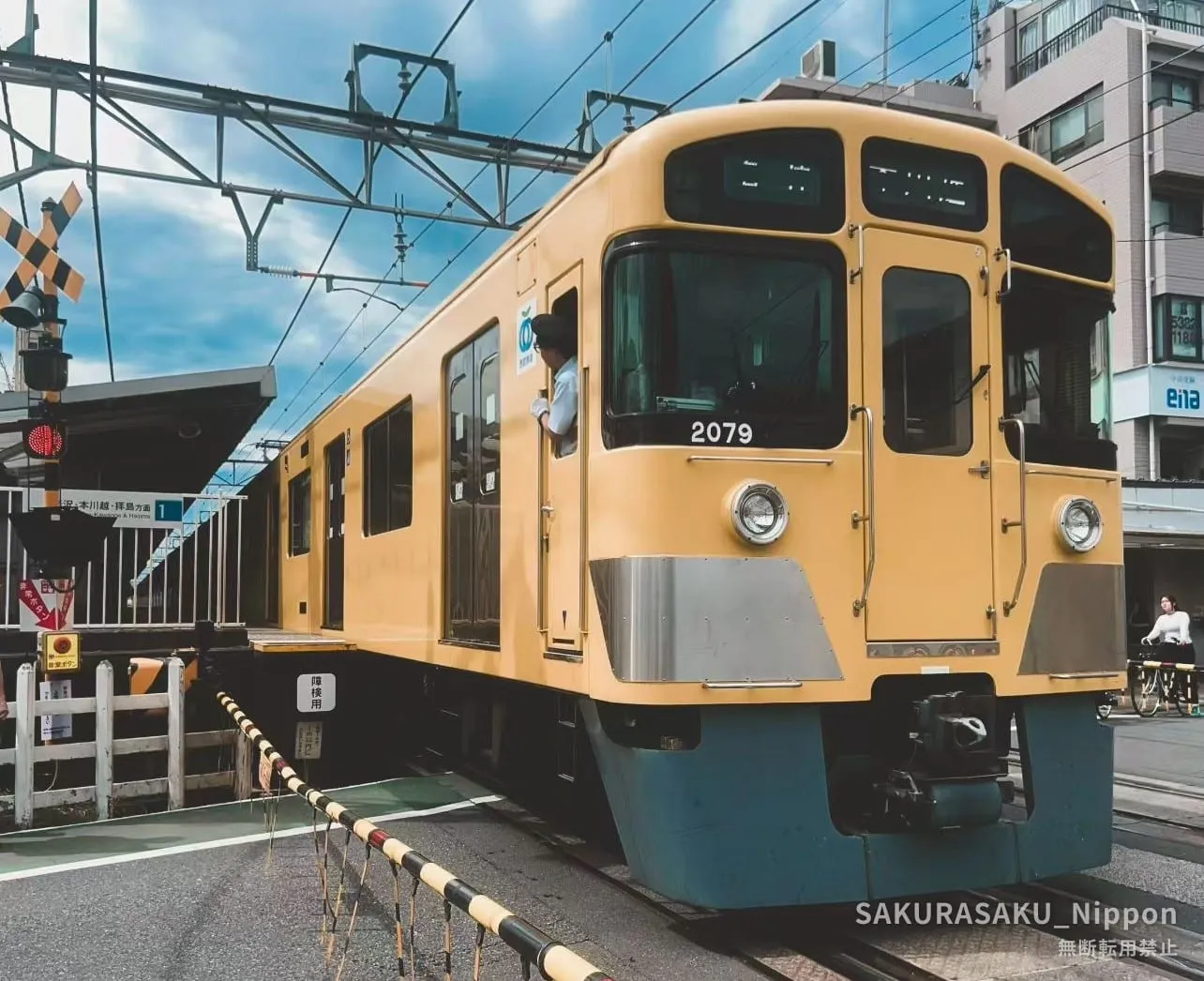 A yellow Seibu Shinjuku Line train stopped beside the level crossing at Kami-Igusa Station