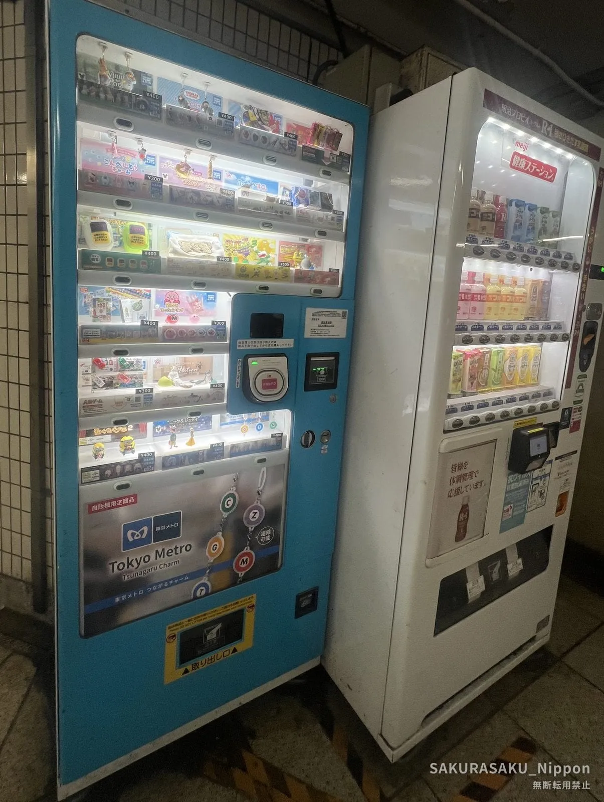 A light-blue vending machine full of small character charms, with a panel for the Tokyo Metro Tsunagaru Charm at the bottom, next to an ordinary drinks machine