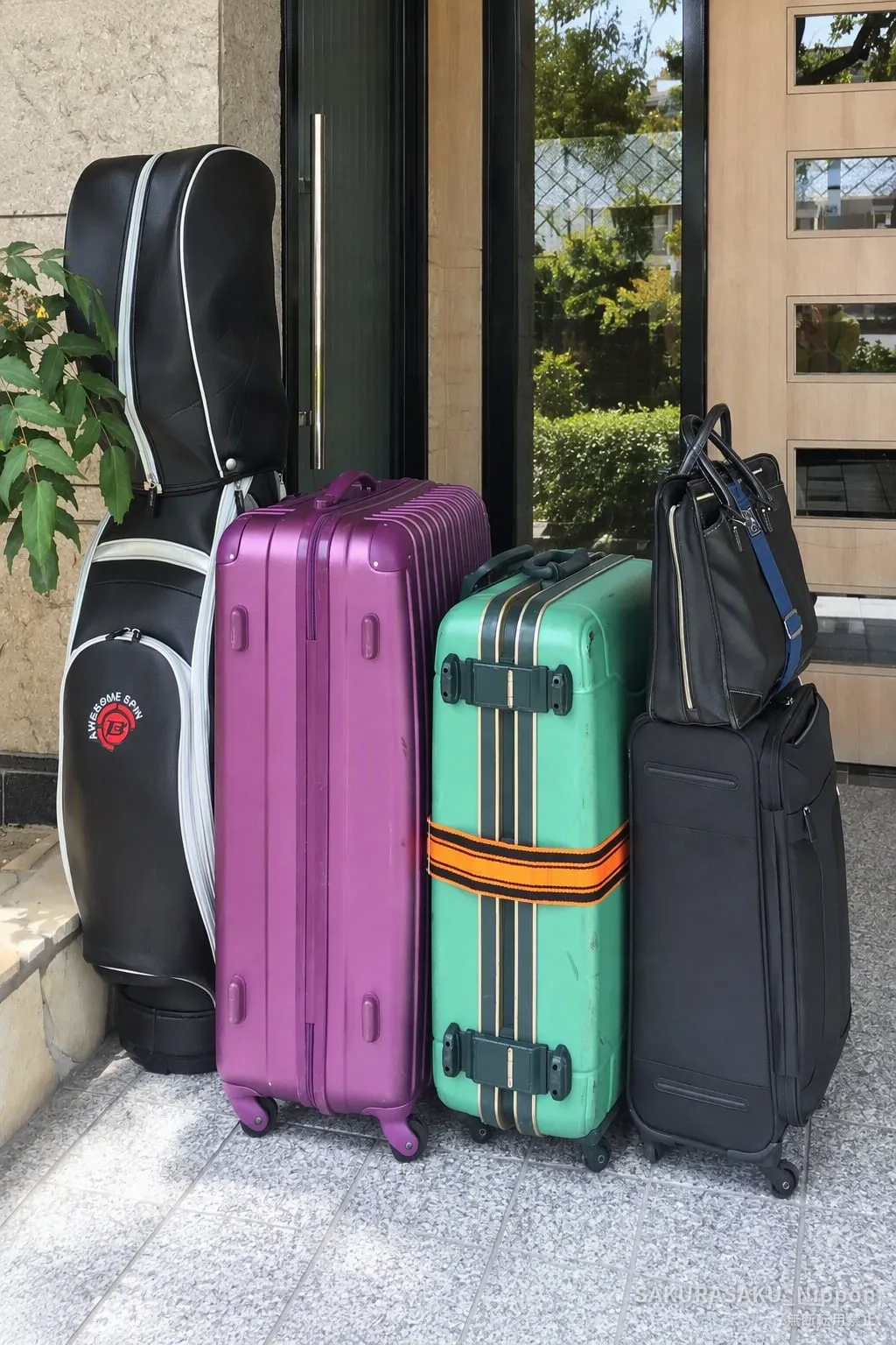 Three suitcases, a golf bag and a tote bag lined up at a front door